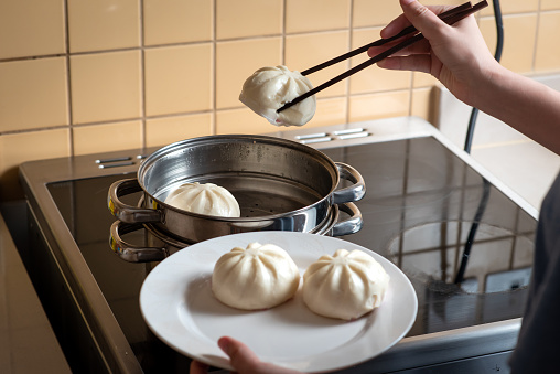 Woman taking out fresh baozi Chinese steamed buns from the metal steamer at home closeup