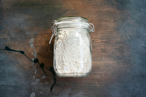 Flour in the glass jar on the wooden kitchen table background top view.