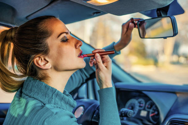 istock Young elegant woman looking in the car view mirror while applying makeup 1257447479
