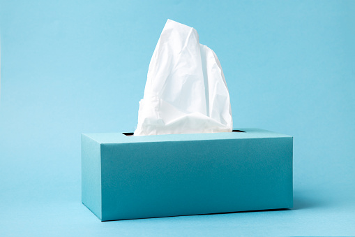 Light blue tissue box on blue background. Cold and flu concept. Minimal monochromatic composition.