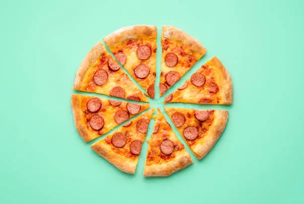 Above view with a sliced pepperoni pizza isolated on a green-mint background. Flat lay with a home-baked pizza salami.