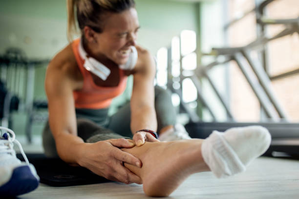 close-up of female athlete feeling pain in her ankle during sports training at health club. - sprain imagens e fotografias de stock