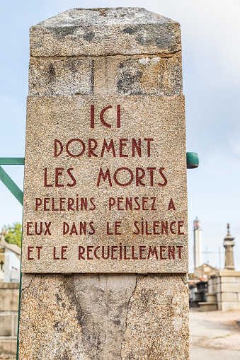 Europe, France, Haute-Vienne, Oradour-sur-Glane. Sept. 5, 2019. Sign saying 'Here Sleep the Dead. Pilgrims think of them in silence and meditation.' In the cemetery of the martyr village.