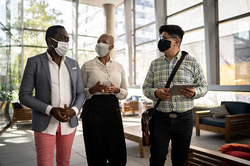 Coworkers walking and talking at office's lobby - with face mask