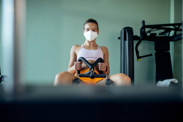 istock Dedicated athletic woman wearing face mask while exercising on roving machine in a gym. 1257454792