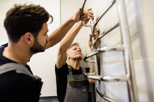 Two plumbers, workers in uniform working, installing towel rail, electric towel dryer on the bathroom wall. Construction, maintenance and repair concept Two plumbers, workers in uniform working, installing towel rail, electric towel dryer on the bathroom wall. Construction, maintenance and repair concept. Selective focus on aged man. Horizontal shot chrome man stock pictures, royalty-free photos & images