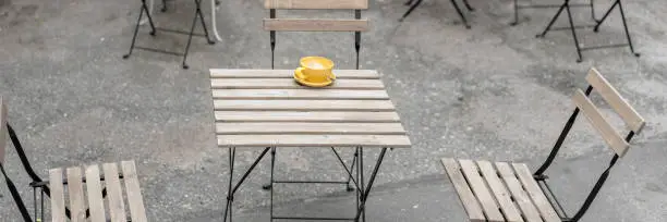 empty street cafe with wooden furniture and lone yellow cup of coffee on table in quarantine time crisis in fast food industry concept outdoors