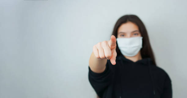 istock girl in mask points with forefinger straight against wall 1257459132