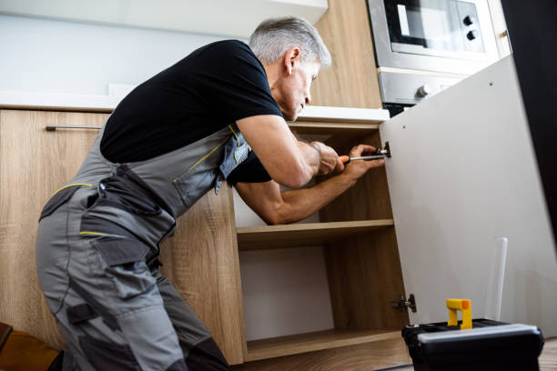 istock Aged repairman in uniform working, fixing kitchen cabinet using screwdriver. Repair service concept 1257460726