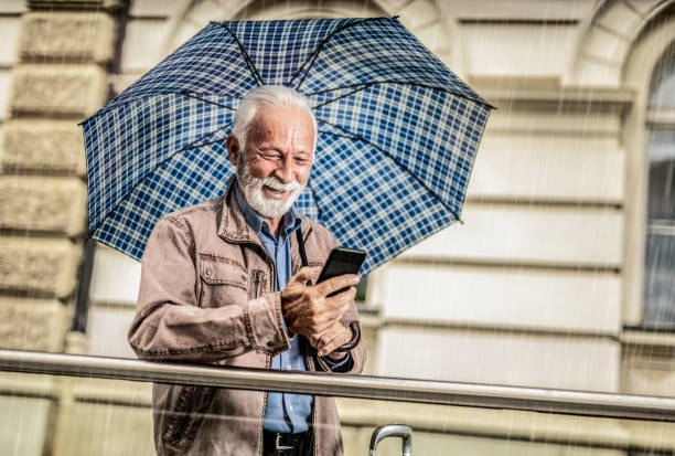 istock Happy senior man using phone under umbrella. 1257461707