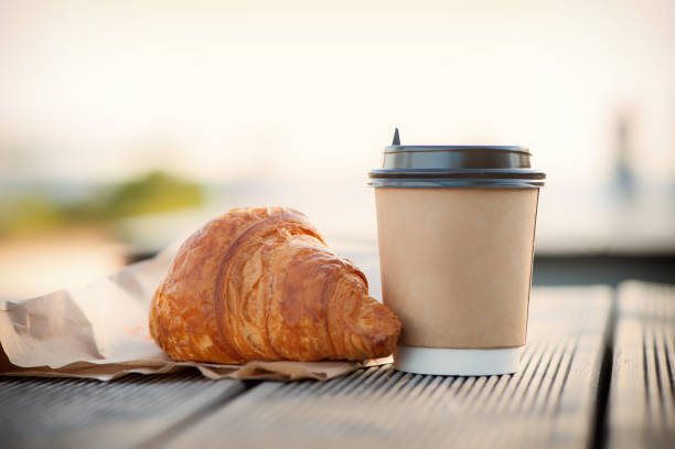 eco paper cup with coffee or tea and croissant on kraft paper, on a wooden table. breakfast on the street, in the park, on a bench. - pastrie imagens e fotografias de stock