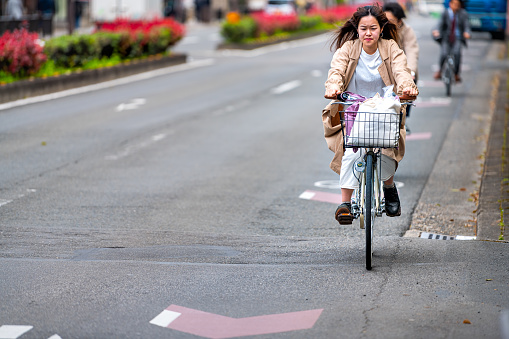 Kyoto, Japan - April 17, 2019: Japanese person woman on bicycle riding bike on street candid city life in traffic road lane