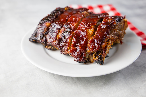 Oven baked barbecue ribs with sauce on a white plate with a red checkered picnic napkin