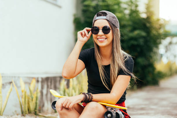 istock Young skateboarder wearing sunglasses and cap sitting on the sidewalk 1257464363