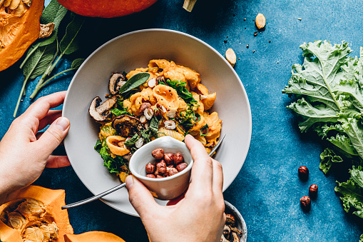 Hand of a woman adding hazelnuts in pasta and pumpkin dish. Female chef making a dish of pasta, pumpkin and mushroom.