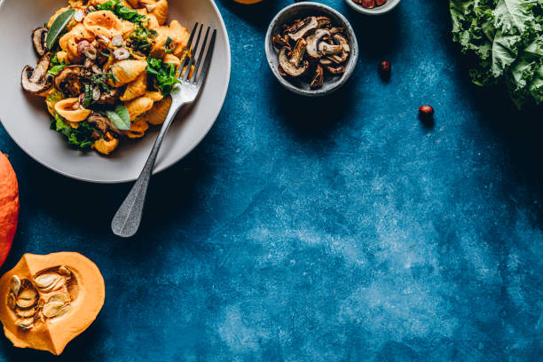 Pumpkin pasta with mushroom and hazelnuts Top view of pumpkin pasta with mushroom and hazelnuts. Autumn meal served in a bowl with ingredients on blue background. food flat lay stock pictures, royalty-free photos & images