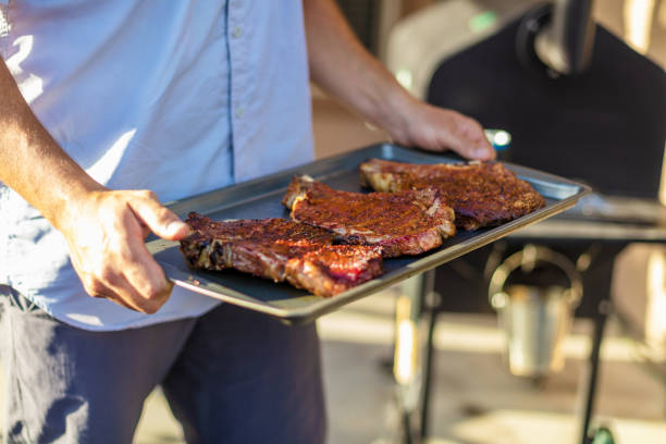 In Western Colorado Millennial Male Carrying Grilled Steak on a Cooking Pan Cookout BBQ Photo Series with Matching 4K Video Available for this BBQ photo Series (Shot with Canon 5DS 50.6mp photos professionally retouched - Lightroom / Photoshop - original size 5792 x 8688 downsampled as needed for clarity and select focus used for dramatic effect)
