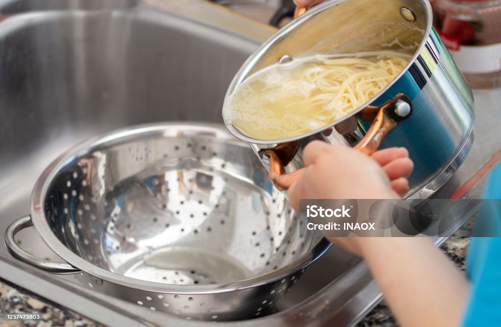 draining the water from the spaghetti woman separating water from spaghetti withempty silver colander Pasta Stock Photo
