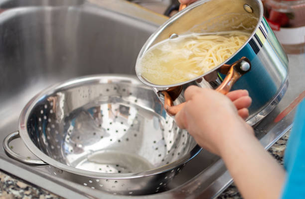 draining the water from the spaghetti - colander imagens e fotografias de stock