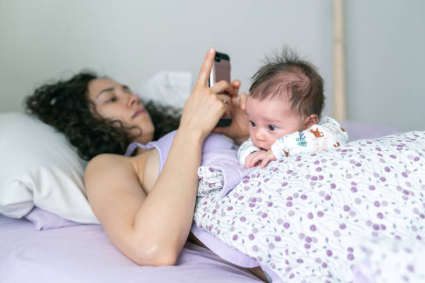 istock Mom on her cell phone while lying in bed with newborn baby 1257482011