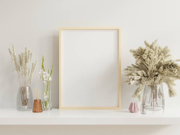 istock Wooden frame leaning on white shelf in bright interior with plants on the table with plants in pots on empty wall background. 1257484790