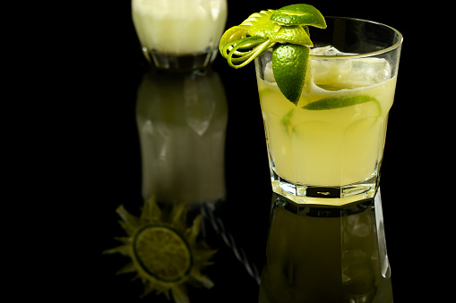 CAIPIRINHA OF LEMON A TYPICALLY BRAZILIAN DRINK, PHOTOGRAPHED ON A DARK GLASS TABLE