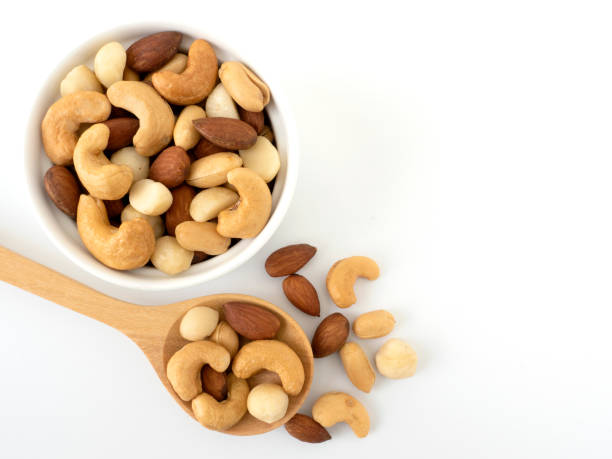 Nuts in top view circle shaped ceramic bowls and nuts on top view wooden spoon isolated on white background. Various nuts (almonds, macadamia, cashew, peanuts). Mix nut healthy ingredients food.