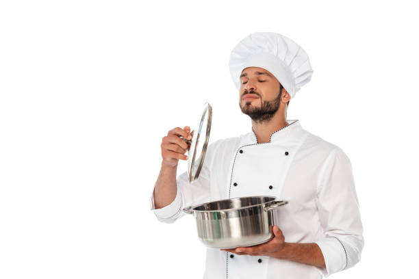 istock Handsome chef with closed eyes holding pan and cap isolated on white 1257500556