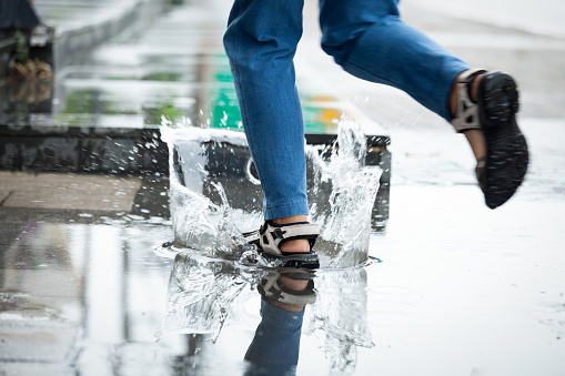 Feet of woman running in puddles with water splash in the rainy day