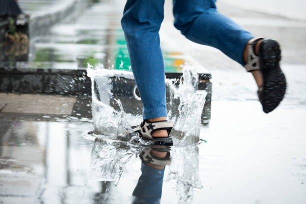 stopy kobiety biegające w kałużach z rozpryskiem wody w deszczowy dzień - puddle street water women zdjęcia i obrazy z banku zdjęć