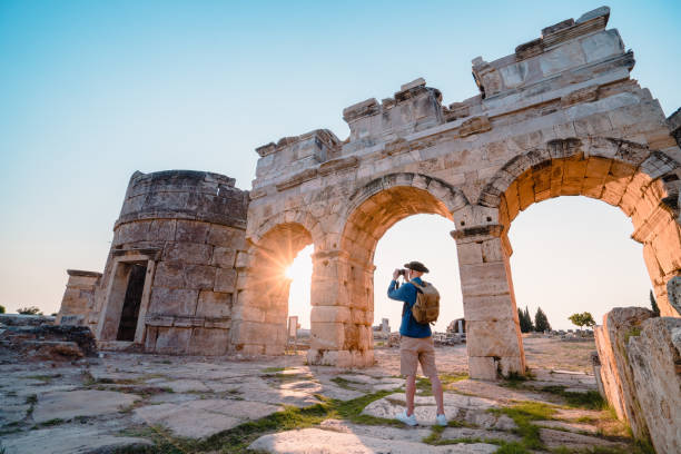 touriste de voyageur prend la photo de la porte de frontinus dans les ruines antiques à hierapolis au coucher du soleil , pamukkale - hierapolis photos et images de collection