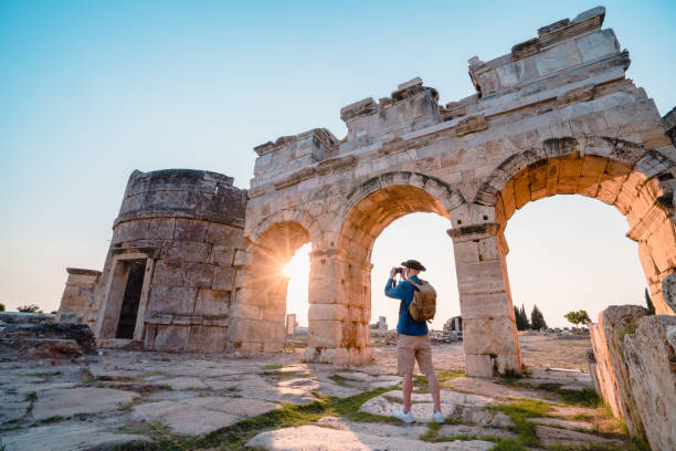 旅行者観光客は夕日にヒエラポリスの古代遺跡でフロンティヌス門の写真を撮っています, パムッカレ - hierapolis ストックフォトと画像