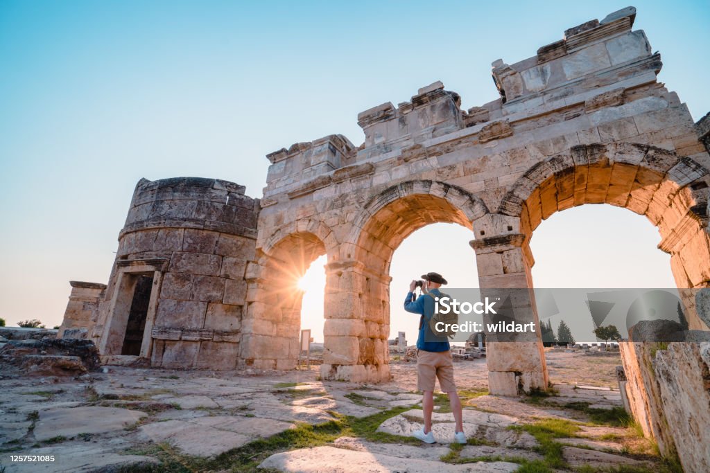 Traveller tourist is taking photo of Frontinus Gate in ancient ruins in Hierapolis at sunset , Pamukkale UNESCO, Photographer, Camera, Travertine pools, Greek architecture Pamukkale Stock Photo