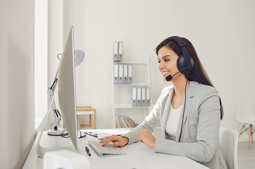 Call center operator woman in headset headphones sitting at a computer in the workplace in modern office. Concept help desk on-line help store