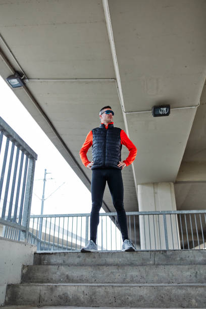 istock Young bearded caucasian man standing with hand on hip and in other hand holding refreshment while taking a break from running. Urban exterior. 1257527634