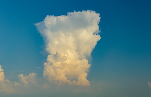 Out of a misty lower cloud layer a huge anvil shaped cumulonimbus cloud tower rises high up in the deep blue sky. A sky only, full-frame and close-up image  with copy space.