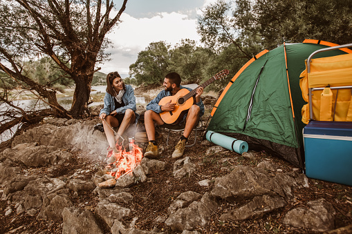 Romantic couple sitting by bonfire. Beautiful couple in love enjoying at campsite.