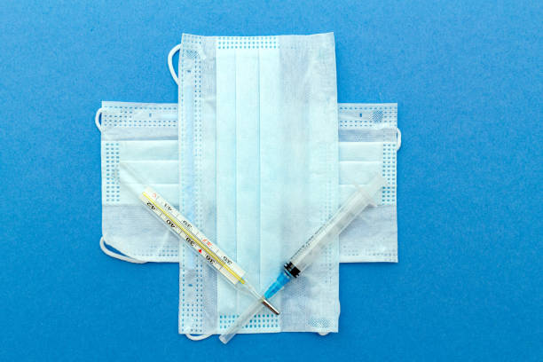 istock medical protective masks cross shape with thermometer, syringe on a blue background with copy space. 1257532272