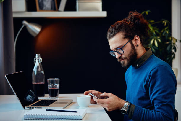istock Side view of serious hipster sitting in his office and using smart phone. 1257532394