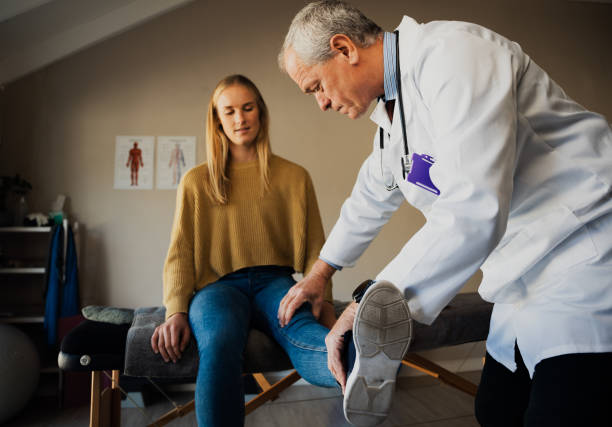 Male Doctor in white coat treating female patients injured knee at rehabilitation centre Caucasian Male Doctor in white coat treating female patients injured knee at rehabilitation centre. High quality photo sports medicine photos stock pictures, royalty-free photos & images