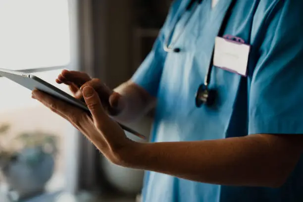 Close-up of female doctor in scrubs with digital tablet, typing and completing checklist. High quality photo