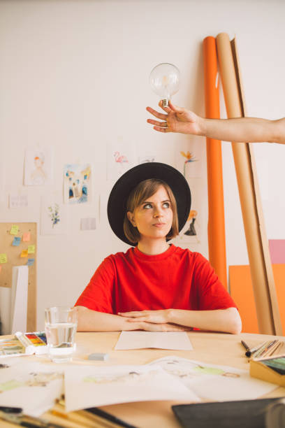 istock Young pretty girl artist in hat thinks and idea comes in studio. Insight is symbolized by a light bulb in hand 1257537862