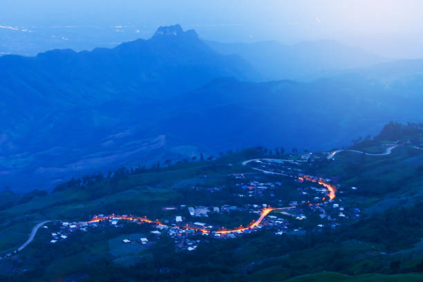 Stunning view of mountain road at sunset, curves asphalt road with light trail from headlights leading through the blue mountains. Phu Thap Boek, Thailand. Long exposure. Soft focus on the road.