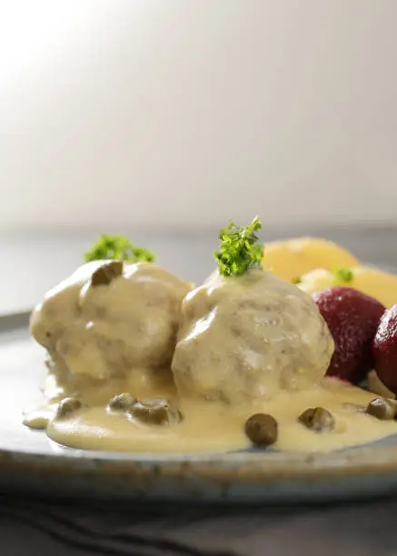 Koenigsberger Klopse or boiled meatballs in white sauce with capers, beetroot potatoes and parsley garnish, traditional in Germany and Poland, copy space, close-up with selected focus, narrow depth of field