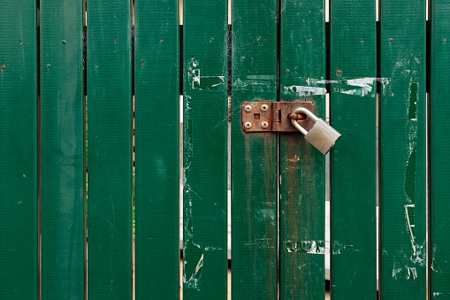 Wooden fence painted dark green with a steel padlock