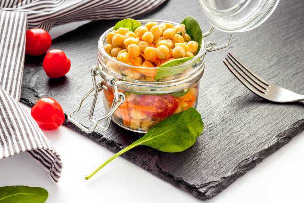 istock Vegan lunch. Chickpeas, carrot, tomato in glass jar on white table 1257556705