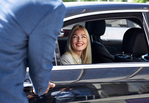 blonde caucasian woman likes customer service in a private taxi, she looks at black male and smile, sits inside of car