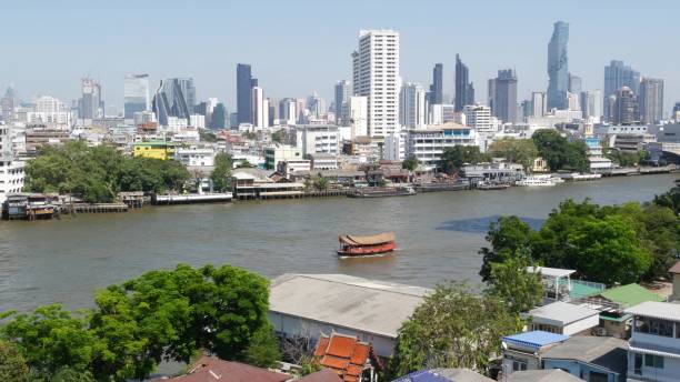 dzielnica finansowa w pobliżu spokojnej rzeki. widok na wieżowce położone nad brzegiem spokojnej rzeki chao praya w centrum bangkoku. panorama życia wielkiego miasta. łodzie na wodzie w krungthep. - krungthep zdjęcia i obrazy z banku zdjęć