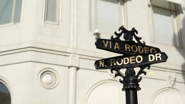 Photo of World famous Rodeo Drive symbol, Cross Street Sign, Intersection in Beverly Hills. Touristic Los Angeles, California, USA. Rich wealthy life consumerism, Luxury brands and high-class stores concept.