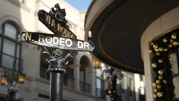 Photo of World famous Rodeo Drive symbol, Cross Street Sign, Intersection in Beverly Hills. Touristic Los Angeles, California, USA. Rich wealthy life consumerism, Luxury brands and high-class stores concept.